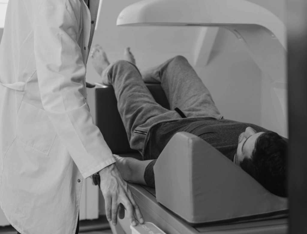 Black and white photo of person sitting on a DEXA scanner with doctor next to him turning starting the machine