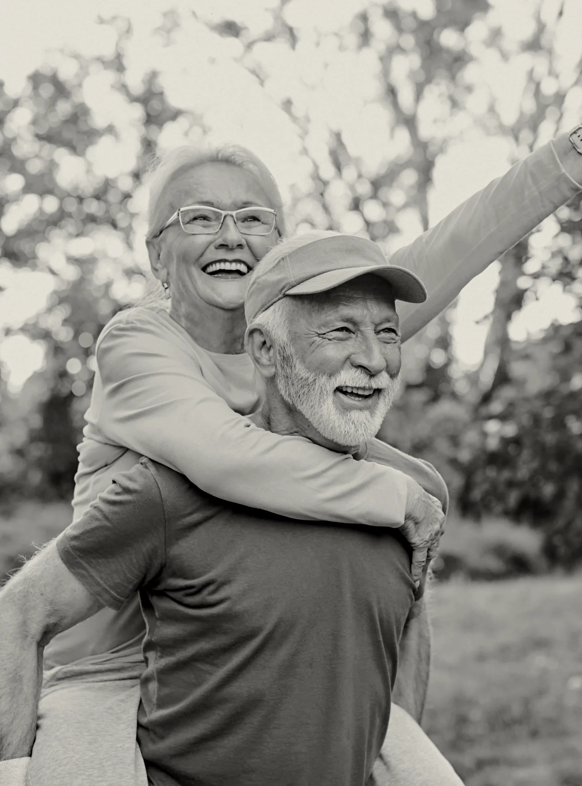 Smiling older couple enjoying time together outdoors, with older women with a arm in the air while on the back of the older mans back
