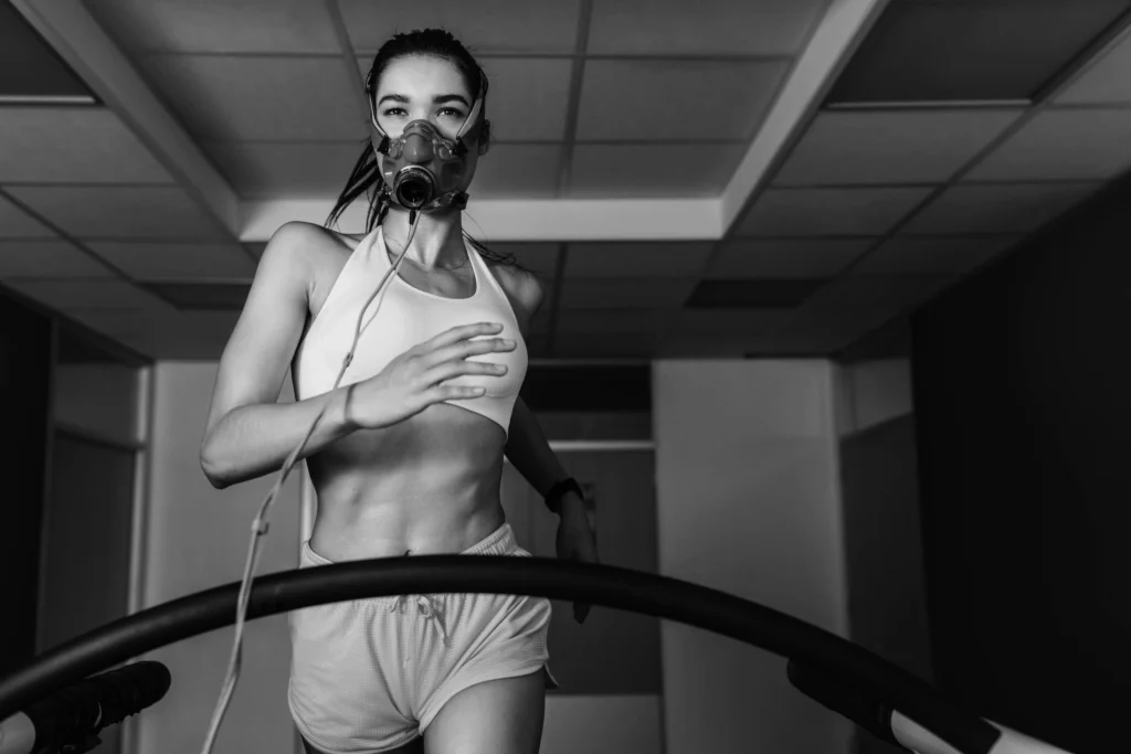 A woman runs on a treadmill while wearing a respiratory mask during a fitness or performance test.